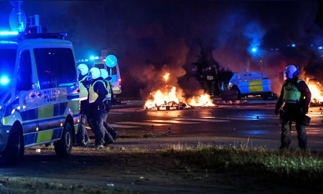 Police officers walk near the burning tyres and pallets during a riot in the Rosengard neighborhood of Malmo, Sweden August 28, 2020. TT News Agency via REUTERS