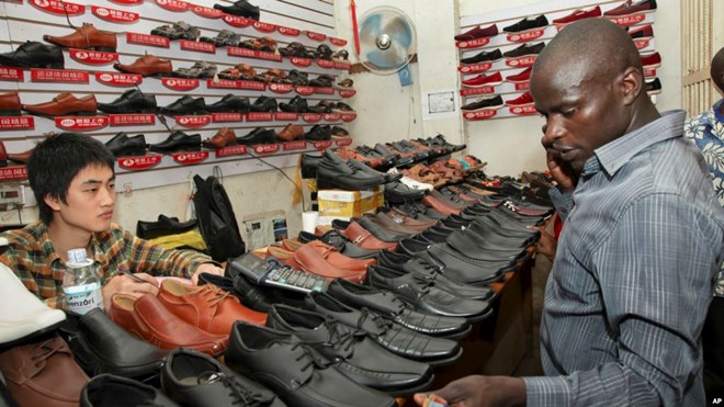 FILE - A Chinese shoe-seller, who declined to give his name, watches as a customer inspects his wares, at a shoe shop in Kampala, Uganda, June 8, 2015. Local merchants have been protesting the presence of Chinese traders, claiming unfair competition.