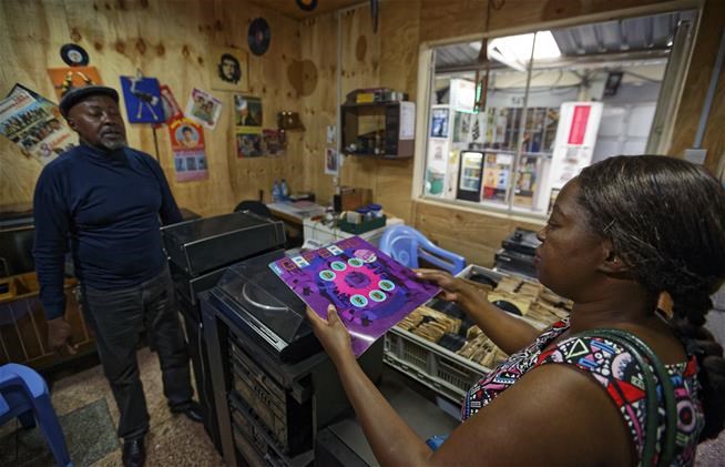 In this photo taken Thursday, March 1, 2018, a potential customer discusses a record with James "Jimmy" Rugami inside his vinyl records stall in Kenyatta Market in Nairobi, Kenya.   (AP Photo/Ben Curtis)